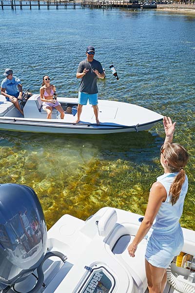 woman tossing beverage from her boat to man standing on an adjacent boat